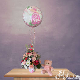 Pink baby girl balloon above a mixed flower arrangement with a teddy bear