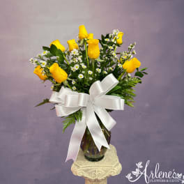 Yellow roses and white daisies in a glass vase with a white ribbon