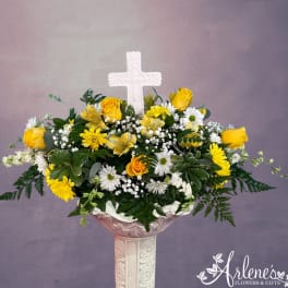 Yellow roses and white daisies in a pedestal vase with a white cross centerpiece