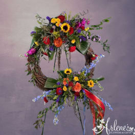 Large double grapevine wreath with bright mixed flowers and ribbons on a stand