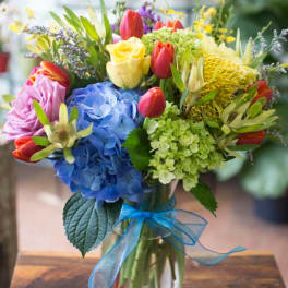 Colorful bouquet with blue hydrangea, yellow rose, red tulips in a glass vase with blue ribbon