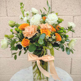 Orange and white flower bouquet in a glass vase with a peach ribbon