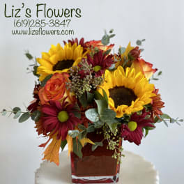 Bouquet of sunflowers, roses, and burgundy daisies in a red glass vase