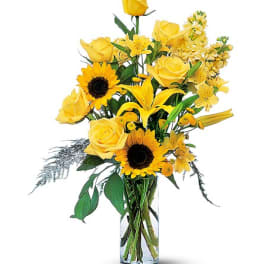 Yellow roses and sunflowers arranged in a clear glass vase