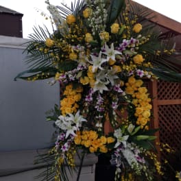 Large standing floral spray with yellow roses, white lilies, and orchids