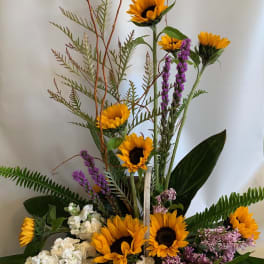 Tall floral arrangement with sunflowers, white blooms, and purple flowers in a square container