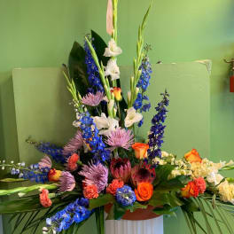 Tall mixed floral arrangement with blue, white, pink, and orange blooms