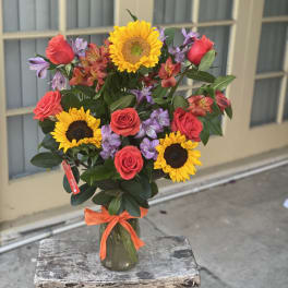 Bouquet of sunflowers, red roses, and purple alstroemeria in a glass vase
