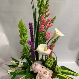 Tall floral arrangement with white calla lilies, pink blooms, and green spikes in a white basket