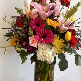 Mixed bouquet in a tall glass vase with lilies, gerberas, roses, and hydrangea