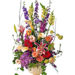 Tall mixed bouquet with roses, lilies, calla lilies, and purple blooms in a cream vase