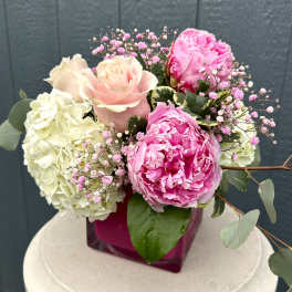 Pink roses and peonies arranged with white hydrangeas in a magenta vase