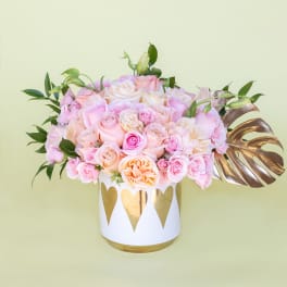 Pink and peach roses arranged in a white vase with gold hearts