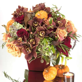 Autumn bouquet with orchids, roses, and small pumpkins in a red vase