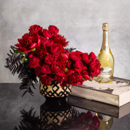 Red rose arrangement in a patterned vase beside a champagne bottle