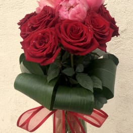 Red and pink roses arranged in a clear glass vase with a red ribbon