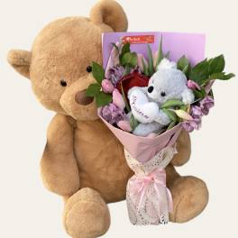 Teddy bear holding a pink bouquet with a small plush bear