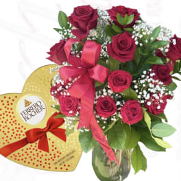 Bouquet of red roses in a glass vase beside a heart-shaped chocolate box
