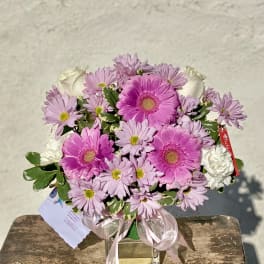 Pink gerberas and daisies arranged in a clear glass vase with a ribbon.