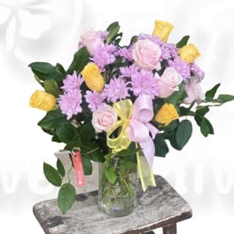 Pink and yellow roses with lavender daisies in a glass vase