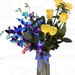 Yellow roses and blue orchids in a glass vase with a blue ribbon.