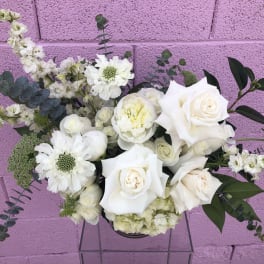 White roses and mixed white flowers in a low arrangement against a pink wall