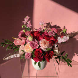 Pink and red rose arrangement in a white vase with tropical accents
