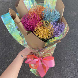 Bouquet of colorful pincushion protea wrapped in brown paper with a pink ribbon