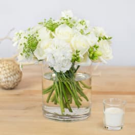 White roses and hydrangeas in a glass vase with a candle nearby