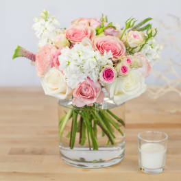 Pink and white rose bouquet in a clear glass vase with a candle beside it