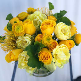 Yellow roses and pale blooms arranged in a clear glass vase