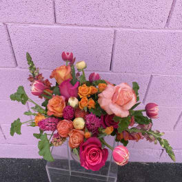 Mixed bouquet of pink, orange, and peach roses in a clear vase