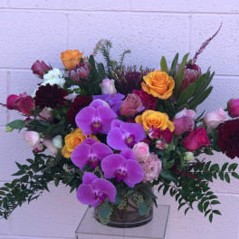 Mixed bouquet with purple orchids, yellow roses, and burgundy blooms in a glass vase