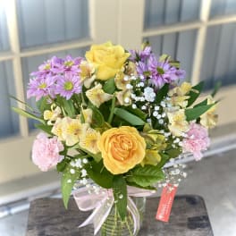 Bouquet of yellow roses, purple daisies, and pink carnations in a glass vase