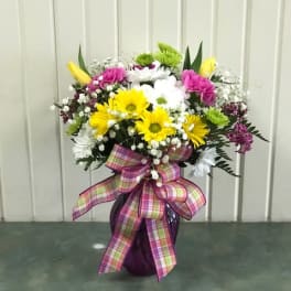 Colorful mixed flower arrangement in a purple vase with a plaid ribbon