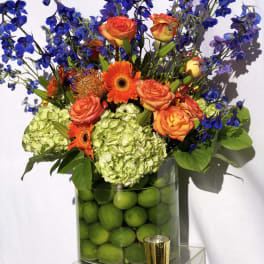 Orange roses and gerbera daisies in a vase with blue flowers
