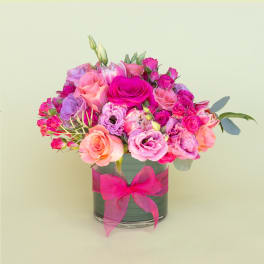 Pink and peach rose bouquet in a glass vase with a pink ribbon
