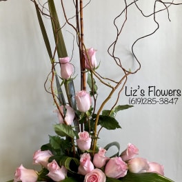 Tall arrangement of pink roses with curly branches and broad leaves