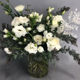 White floral arrangement in a glass vase with dark foliage