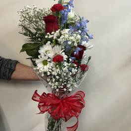 Bouquet of red roses, white daisies, and blue flowers wrapped with a red ribbon