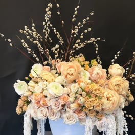 Large peach and cream floral arrangement in a white vase with tall branches