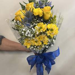 Bouquet of yellow roses and blue thistle wrapped in clear plastic with a blue bow