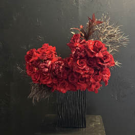 Red rose arrangement in a black vase with dark foliage