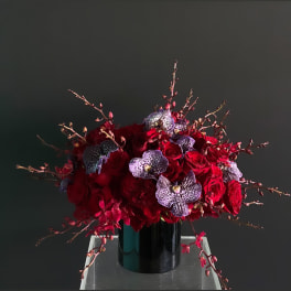 Red rose arrangement with spotted orchids in a black vase