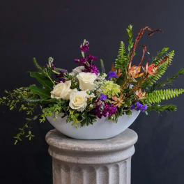 White roses and purple flowers in a low white bowl vase