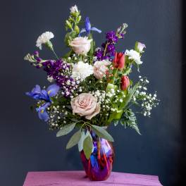 Mixed bouquet of roses, tulips, irises, and carnations in a glass vase