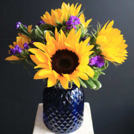 Sunflowers and purple filler flowers in a blue glass vase