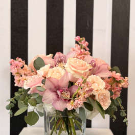 Pink roses and orchids arranged in a clear square vase.