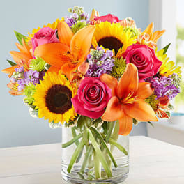 Bouquet of sunflowers, pink roses, and orange lilies in a glass vase