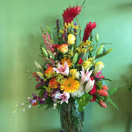Tall mixed bouquet in a glass vase with lilies, roses, and gerbera daisies